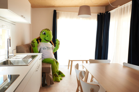 En stor skildpadde-maskot sidder i stuen i Els Pins- Mobile-Home Plus 2 i Spanien med lyst interiør.