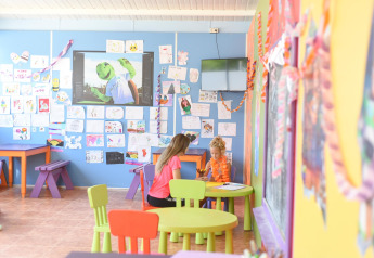 Zona de juegos para niños en glamping, mesas y sillas coloridas, paredes decoradas con dibujos infantiles.