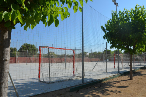 Outdoor sports field at a glamping site, surrounded by trees and netted fencing under a clear sky.