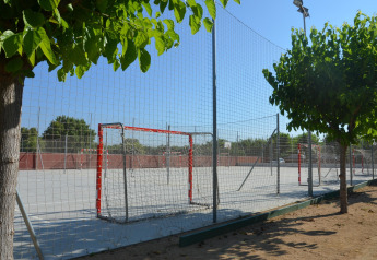 Campo deportivo al aire libre en un alojamiento glamping, rodeado de árboles y vallado de red al sol.