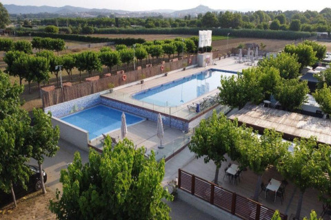 Outdoor swimming pool area at a glamping site with lounge chairs, surrounded by trees and scenic fields.
