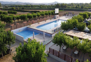 Outdoor swimming pool area at a glamping site with lounge chairs, surrounded by trees and scenic fields.