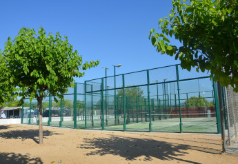 Pista de pádel junto a zona de mobil home, rodeada de árboles verdes y cielo azul para actividades.