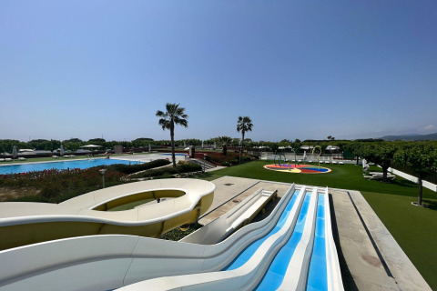 Foto af et luksuriøst glamping-resort med pools, vandrutsjebaner og grønne områder under en klar himmel.