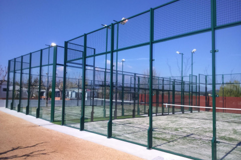 Udendørs padelbane med høje hegn og belysning under blå himmel ved et glampingsted i naturen.