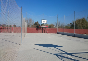 Cancha deportiva al aire libre en un alojamiento glamping, con aro de baloncesto y portería, rodeada de red.