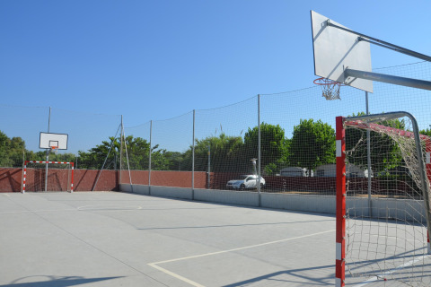 Udendørs multibane på glampingsted med basketballkurv og mål, solskinsvejr og grønne omgivelser.