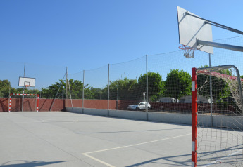 Cancha deportiva multiusos al aire libre en un glamping con aro de baloncesto, portería y día soleado.