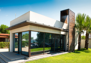 Moderne glamping-indkvartering med store vinduer, hvid facade og træelementer omgivet af grøn have.
