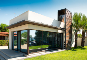 Alojamiento glamping moderno con grandes ventanales, fachada blanca y detalles de madera rodeado de césped.