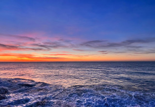 Smuk udsigt over havet ved solnedgang set fra et glampingophold, himlen i blå og orange nuancer.