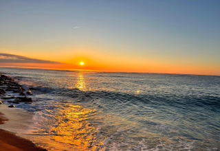 Stunning sunset over the ocean viewed from a glamping site, sunlight reflecting on calm blue water.