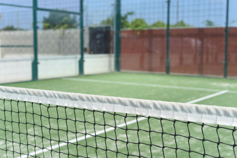 Padeltennisbane med hegn og net, fotograferet på et glampingsted under en solrig himmel med grøn baggrund.