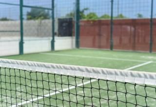 Padeltennisbane med hegn og net, fotograferet på et glampingsted under en solrig himmel med grøn baggrund.