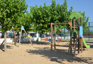 Playground with swings, climbing frame, and slide under trees at a glamping site on a sunny day.