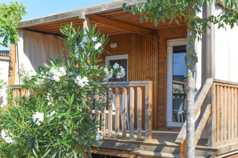 Mobilhome Els Pins-Mobile-Home Plus 3 i Spanien med træveranda, blomstrende buske og træer foran.