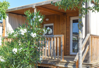 Mobilhome Els Pins-Mobile-Home Plus 3 i Spanien med træveranda, blomstrende buske og træer foran.