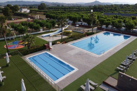 Udendørs swimmingpool og vandrutsjebaner ved Els Pins Mobile-Home Plus 3 i Spanien, omgivet af grønne områder.