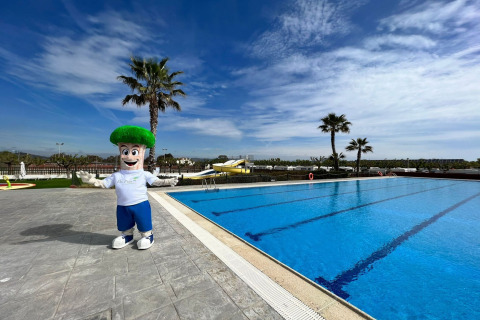 Maskot poserer ved udendørs swimmingpool ved Els Pins- Mobile-Home Plus 3 under blå himmel i Spanien.