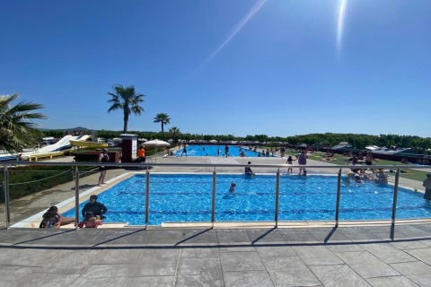 Udendørs poolområde ved Els Pins- Mobile-Home Plus 3 i Spanien med børn og voksne, sol og palmer.