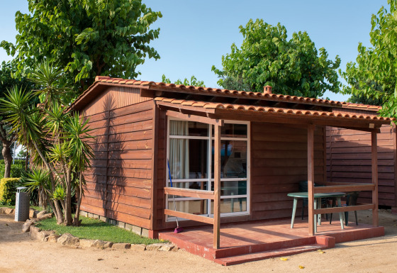 Wooden bungalow with veranda at Els Pins- Bungalow Comfort, surrounded by lush greenery and trees.