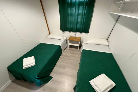 Simple lodge room at Els Pins- Bungalow Comfort in Spain, with twin beds, green covers, and a small nightstand.