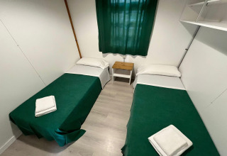 Simple lodge room at Els Pins- Bungalow Comfort in Spain, with twin beds, green covers, and a small nightstand.