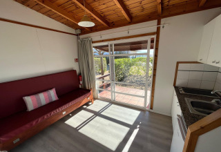 Interior view of Els Pins-Bungalow Comfort lodge in Spain, showing sofa, kitchenette and garden view.