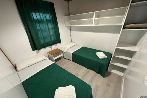 Room at Els Pins- Bungalow Comfort in Spain featuring two single beds, green curtains, and wall shelves.