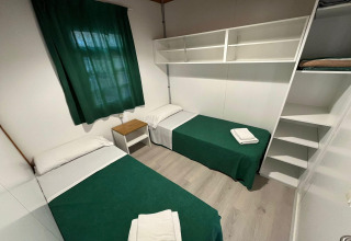 Room at Els Pins- Bungalow Comfort in Spain featuring two single beds, green curtains, and wall shelves.