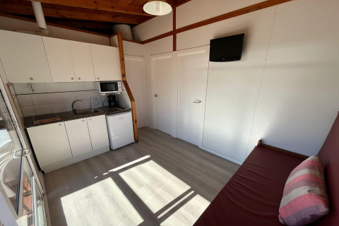 Compact kitchen and living area at Els Pins Bungalow Comfort, Spain, with sofa, TV, and white cabinets.