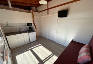 Compact kitchen and living area at Els Pins Bungalow Comfort, Spain, with sofa, TV, and white cabinets.
