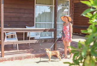 Woman in sunhat with dog on leash standing outside wooden bungalow at Els Pins- Bungalow Comfort, Spain.