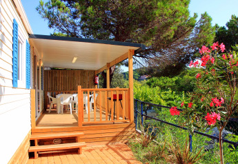 Mobilhome med overdækket terrasse, bord og stole i grønne omgivelser ved Camping Rocagrossa, Spanien.