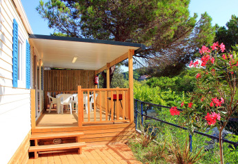 Mobil-home avec terrasse couverte, table de jardin et fleurs au Camping Rocagrossa en Espagne, cadre verdoyant.