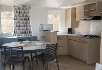 Cocina y comedor modernos de mobil home en España, muebles de madera, mesa para seis y cortinas coloridas.