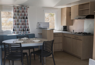 Cucina e zona pranzo moderna in una casa mobile in Spagna, mobili in legno, tavolo per sei e tende colorate.