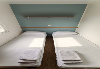 Twee eenpersoonsbedden met witte lakens en handdoeken in een mobilhome op Camping Rocagrossa, Spanje.