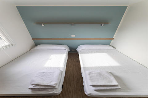 Twee eenpersoonsbedden met witte lakens en handdoeken in een mobilhome op Camping Rocagrossa, Spanje.