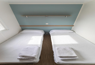 Due letti singoli con lenzuola e asciugamani bianchi in una casa mobile al Camping Rocagrossa, Spagna.