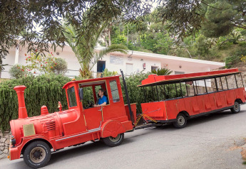 Tren turístico rojo con conductor frente a zona verde de mobil home en Camping Rocagrossa, España.