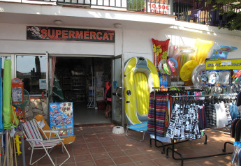 Entrée du supermarché à Camping Rocagrossa en Espagne, avec matériel de plage, bouées et vêtements à l'extérieur.