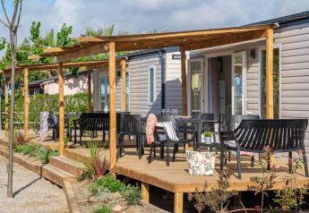 Casa móvil con terraza de madera y sillas negras en CAMPING ESTIVAL VENDRELL PLATJA mediterráneo para 4 personas.
