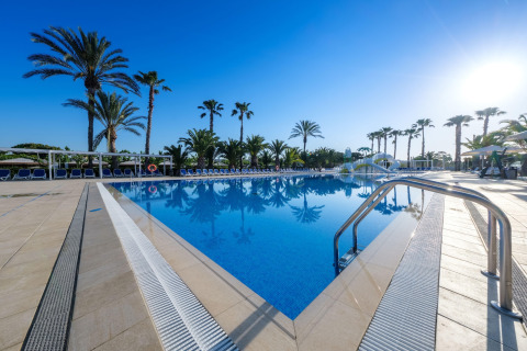 Gran piscina rodeada de palmeras y tumbonas bajo un cielo soleado en un alojamiento de glamping lujoso.
