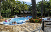 Area piscina all'aperto con palme e persone che si rilassano, fotografata in una sistemazione glamping.