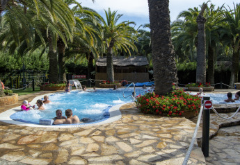 Area piscina all'aperto con palme e persone che si rilassano, fotografata in una sistemazione glamping.