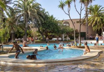 Famiglie che si divertono in una piscina all'aperto circondata da palme in una struttura glamping in una giornata di sole.