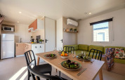 Casa mobile moderna con cucina, tavolo da pranzo per quattro e divano verde al Camping Estival Vendrell Platja.