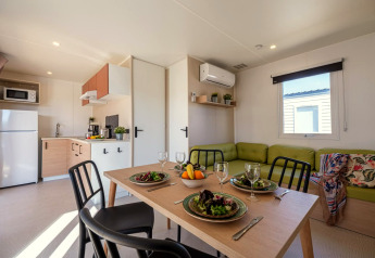 Modern mobile home interior with kitchen, dining table for four, and green sofa at Camping Estival Vendrell Platja.