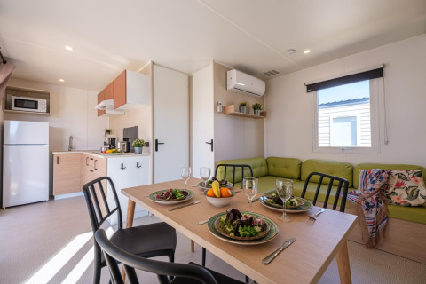 Moderne stacaravan met keuken, eettafel voor vier en groene bank bij Camping Estival Vendrell Platja.